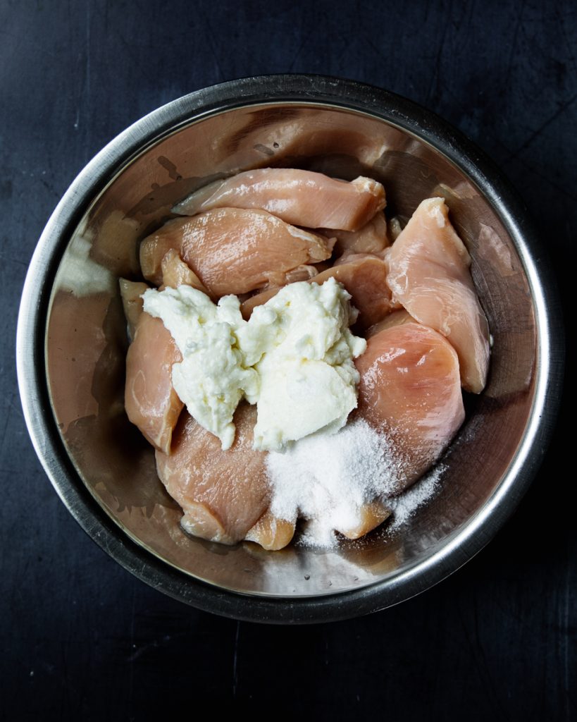 raw chicken breasts in a bowl with toum and salt