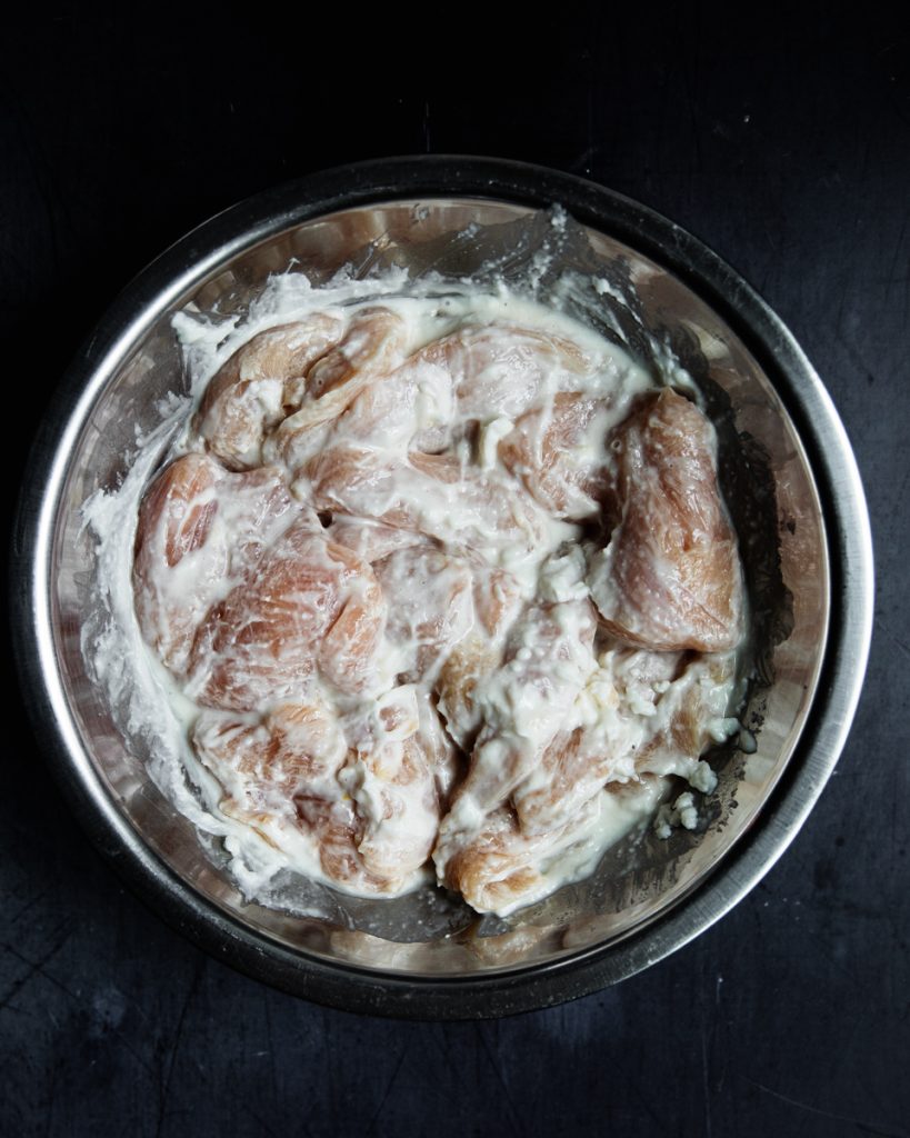 raw chicken breasts in a bowl mixed with toum and salt