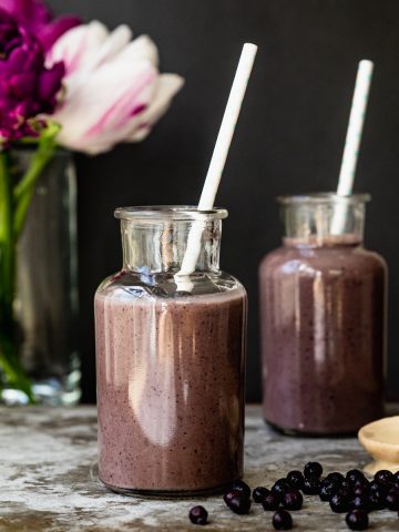 shot of two glasses with smoothie and straw. flowers in background, blueberries on foreground